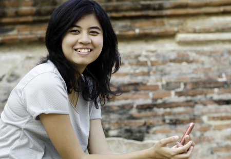 Smiling woman holds her phone with brick backgroundの写真素材