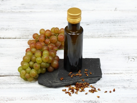 Grape seed oil from  grape seeds in a brown bottle , grape seeds in front and  fresh grapes on wooden tableの写真素材