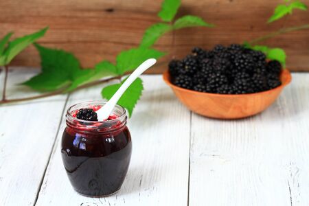 Fresh homemade blackberry jam in a jar.   Decorated with blackberry branch on white wooden table.の写真素材