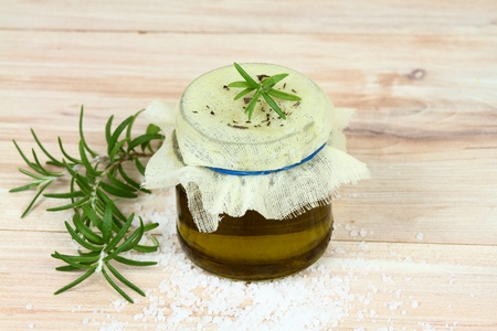 Filtering homemade organic rosemary oil.  Natural remedy, oil and fresh rosemary leaves on wooden background.の写真素材