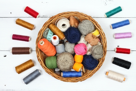 Composition with treads, cottons and sewing accessories. Colored sewing threads in a basket on white...