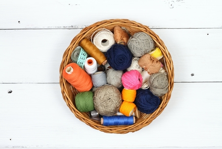 Composition with treads, cottons and sewing accessories. Colored sewing threads in a basket on white...