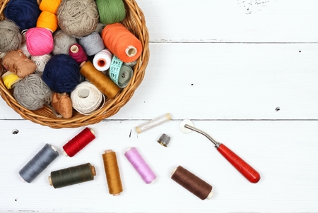 Composition with treads, cottons and sewing accessories. Colored sewing threads in a basket on white...