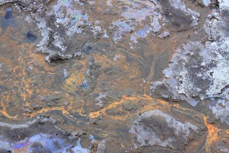 Drying out lake bed in the winter. Colorful oil stains, mud and ice on the bottom.