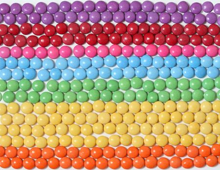 Colorful and sweet smarties background. Chocolate buttons in lines and colors of rainbow.  