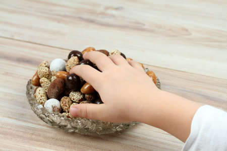 Child hand taking assorted chocolate and coated candies. Delicious sweets placed in a bowl on the wooden table.の写真素材