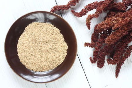 Amaranth seeds on brown plate and dried red flower on white wooden table. Used for gluten free diet, flat lay.の写真素材