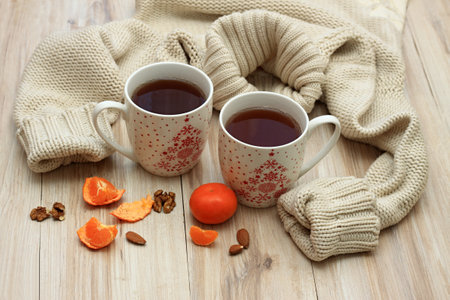 Winter concept with tea for two, sweater and tangerines. Two big mugs with tea surrounded by warm knitted sweater on wooden table.の写真素材