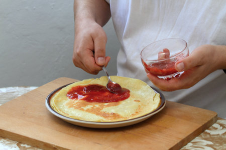 Man's hands and pancakes with strawberry jam. Young cook decorating pancakes with sweet stawberry jam.の写真素材