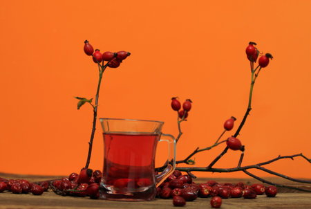 Rosehip tea tea full of vitamins on wood table. Autumn mood and colors come from fresh rosehips, november leaves and orange background.の写真素材