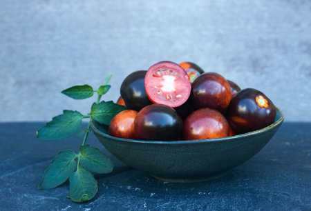 Black tomatoes of Indigo Rose in a bowl on the stone table. This natural form is rich in anthocyanin in black peel and good for our health.の写真素材