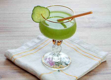 Delicious smoothie  from cucumbers in glass decorated with gold on wooden table. Cucumber drink made from fresh cucumbers,  embroidered napkin on wooden table.の写真素材