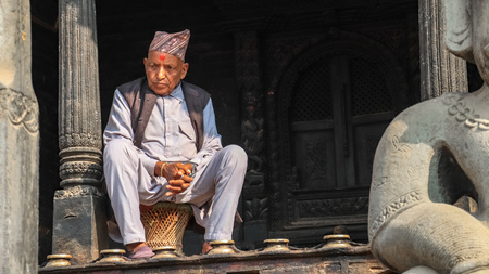 Bhaktapur, Nepal - December 8 2018: An elderly Nepali man sitting infront of a templeのeditorial素材