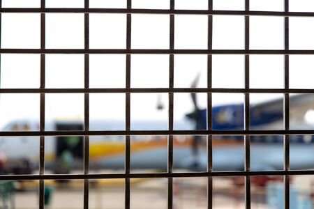 Close up pattern of metal grid fence. Airplane on the runway at background.