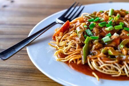 American Chopsuey served in a white plate on wooden surfaceの写真素材