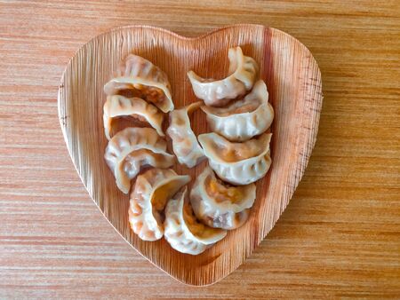 Momo served in a heart-shaped plate placed on a wooden surface.の写真素材