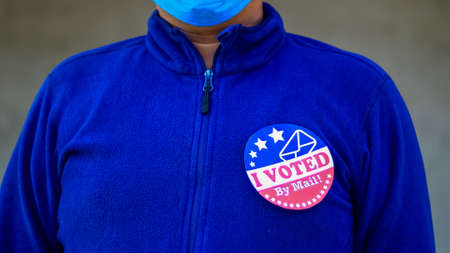 Man in mask from minority group produly holds Voted By Mail sticker during US Election closeup.の写真素材