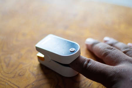 Pulse Oximeter to measure oxygen saturation level in body. Asian male hands puts index finger inside portable oximeter to measure oxygen level.の写真素材