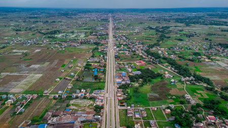 Aerial view of six-lane highway passing through meadows, fields and scattered houses towards mountains in countryside Nepal.の写真素材