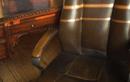 A close up of a old leather office chair and wood desk during sunset.の写真素材