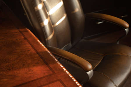 A close up of a old leather office chair and wood desk during sunset.の写真素材