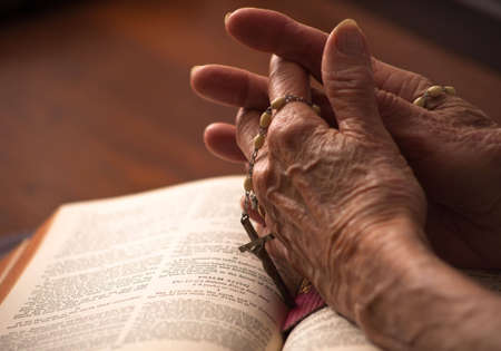 A close up of a senior womans hands on the bible with rosary.の写真素材