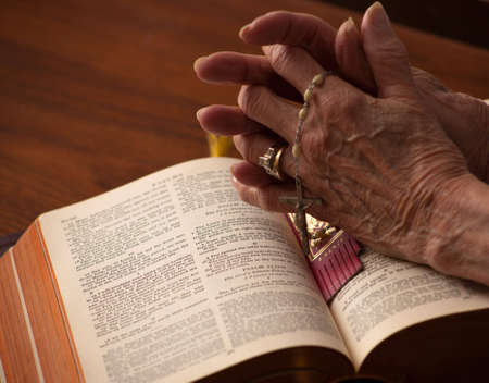 A close up of a senior womans hands on the bible with rosary.の写真素材