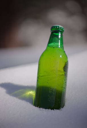 A close up of a green beer bottle sitting in snow.の写真素材
