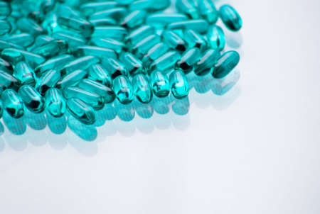 A close up of a bunch of turquoise pills with a white glass background.