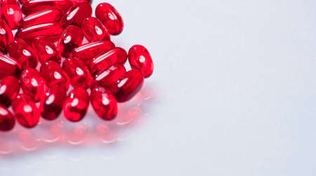 A close up of a bunch of red pills with a white glass background.の写真素材