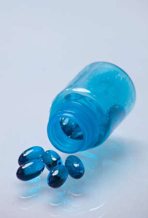 A close up of a bunch of blue pills coming out of a blue bottle with a white glass background.の写真素材