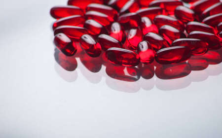 A close up of a bunch of red pills with a white glass background.の写真素材