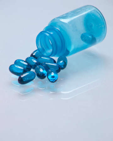 A close up of a bunch of blue pills coming out of a blue bottle with a white glass background.の写真素材