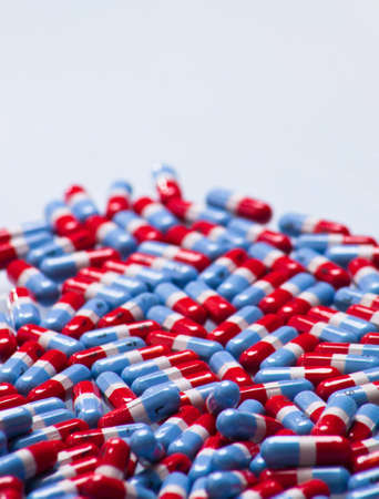 A close up of a bunch of red, gray and blue pills with a white glass background.の写真素材