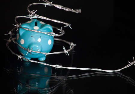 A close up of a blue piggy bank surrounded by barbed wire with a black background.