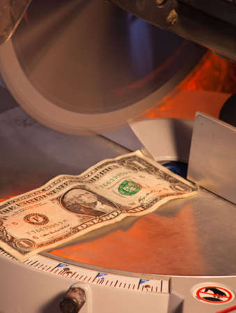 A close up of a dollar under a saw blade.の写真素材