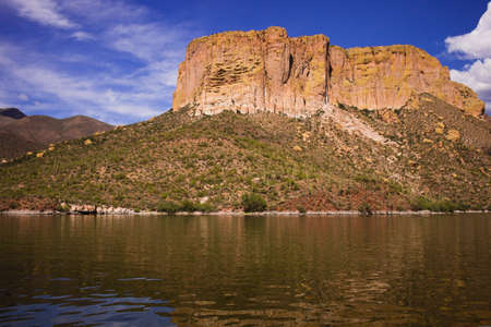 A shot of desert rock with a blue sky and clouds and a lake.の写真素材