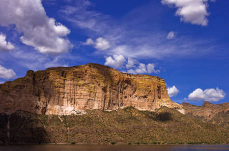 A shot of desert rock with a blue sky and clouds and a lake.の写真素材