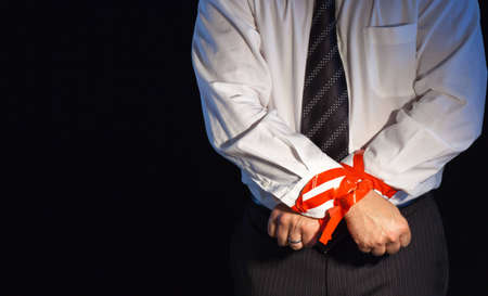 A close up of a man in a suite with his hands tied up with red tape.の写真素材