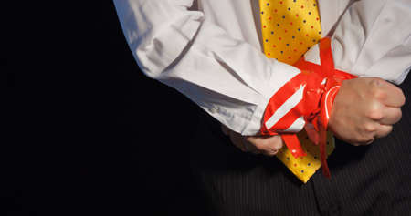 A close up of a man in a suite with his hands tied up with red tape.