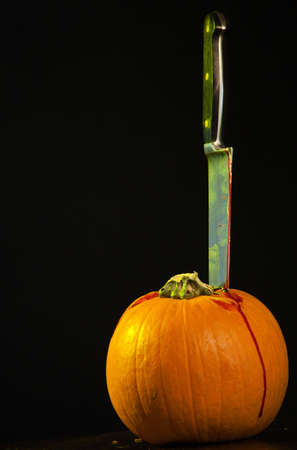 A close up of a pumpkin on a old wooden table with a bloody  knife stuck in the top of the pumpkin.の写真素材
