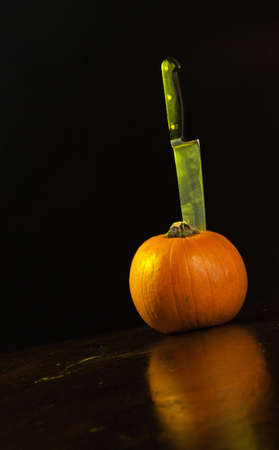 A close up of a pumpkin on a old wooden table with a knife stuck in the top of the pumpkin.の写真素材