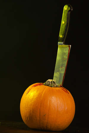 A close up of a pumpkin on a old wooden table with a bloody  knife stuck in the top of the pumpkin.の写真素材