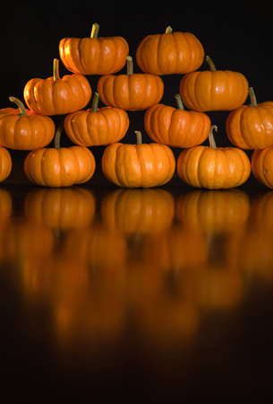 A shot of a bunch of mini pumpkin's stacked in a pyramid wit a black  background.の写真素材