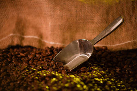 A close up of a metal coffee scooper sticking out of a burlap bag of coffee beansの写真素材
