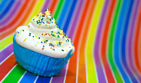 A close up of a blue cupcake with whit frosting sitting on a rainbow striped background.の写真素材