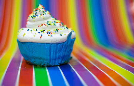 A close up of a blue cupcake with whit frosting sitting on a rainbow striped background.の写真素材