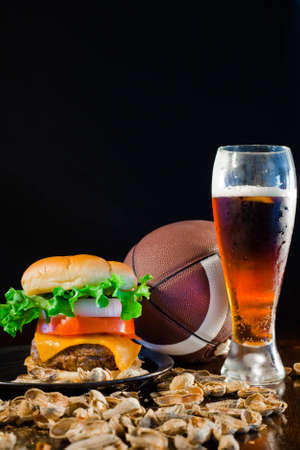 A close up of a big hamburger surrounded with peanuts, beer and a football.の写真素材