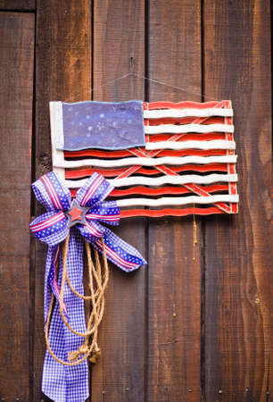 A close up of an old wood US flag with a red, white and blue star ribbon hanging on a wood wall.の写真素材