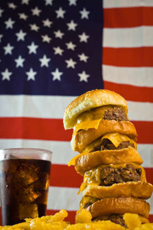A close up of a five patty cheese burger, fries, iced soda and US flag in the background.の写真素材